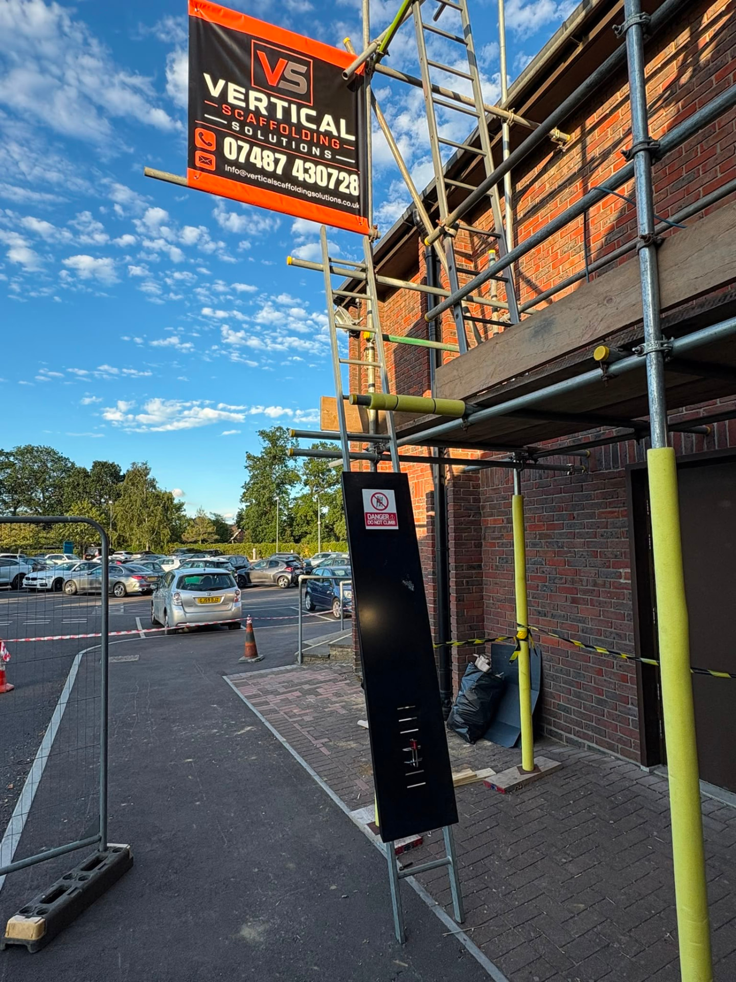 Commercial scaffolding with Vertical Scaffolding Solutions banner and safety signage